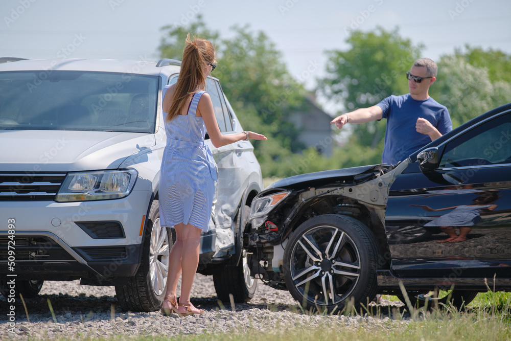 Naklejka premium Angry woman and man drivers of heavily damaged vehicles arguing who is guilty in car crash accident on street side. Road safety and insurance concept