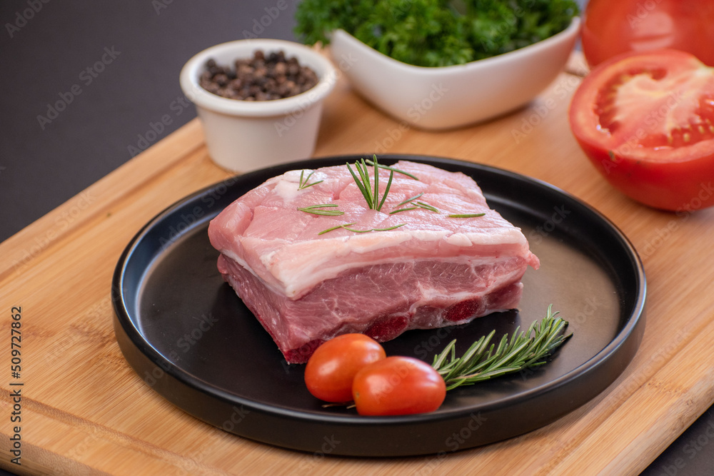 A piece of raw pork with rosemary leaf and cherry tomato and black pepper