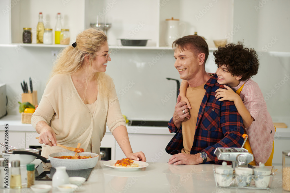 Happy woman adding bolognese sauce on top of portion of homemade pasta she cooked for family Happy woman adding bolognese sauce on top of portion of homemade pasta she cooked for family