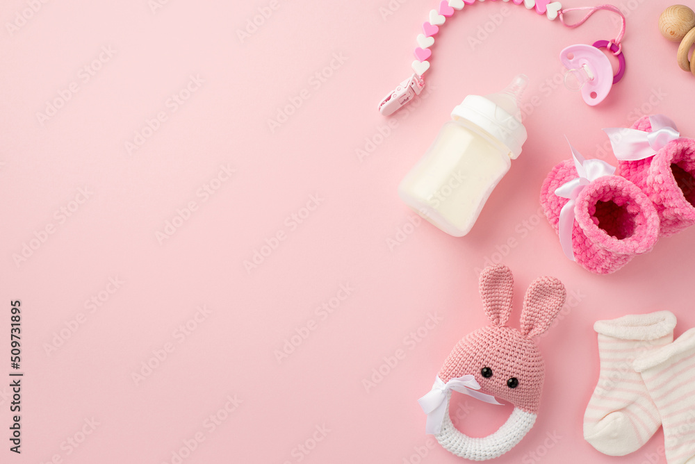 Baby accessories concept. Top view photo of tiny pink shoes socks knitted bunny rattle toy pacifier chain wooden rattle and bottle on isolated pastel pink background with copyspace