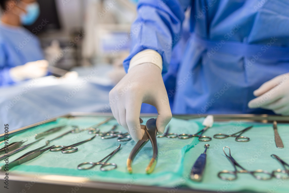 Operating Room of Surgical Table with Instruments, Assistant Picks up Instruments for Surgeons During Operation. Surgery in Progress. Professional Medical Doctors Performing Surgery. Operating Room of Surgical Table with Instruments, Assistant Picks up Instruments for Surgeons During Operation. Surgery in Progress. Professional Medical Doctors Performing Surgery.