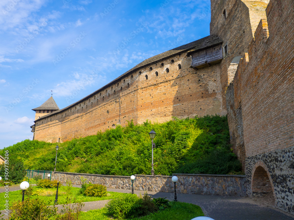 Lutsk High Castle, also known as Lubart's Castle. Ukraine. Brick Tower and Wall. A part of defence wall of Lutsk Castle. The Lord's Tower against the blue sky and with greenery under a brick wall.