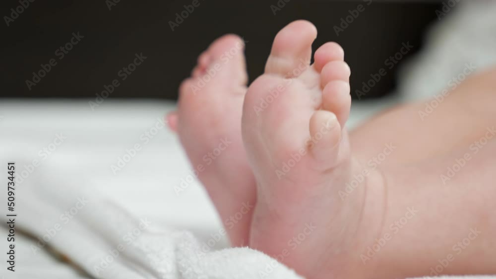 Barefoot newborn girl lies on white sheet laid on bed making careful moves. Plump baby with bare legs and soft skin rests in bedroom at home closeup Barefoot newborn girl lies on white sheet laid on bed making careful moves. Plump baby with bare legs and soft skin rests in bedroom at home closeup