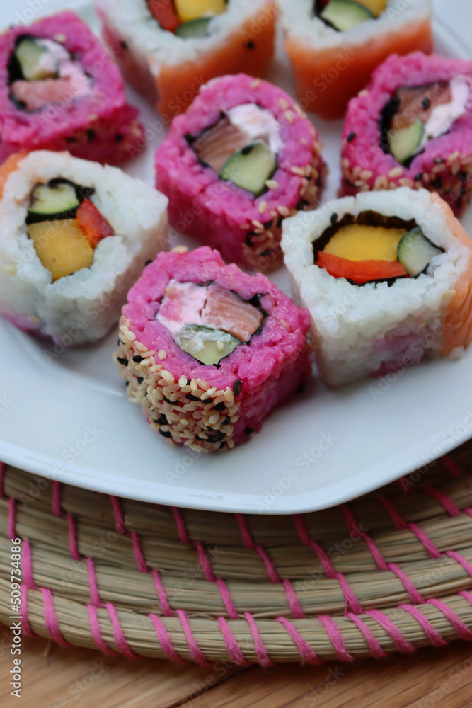 Japanese salmon sushi colored with beetroot juice with inside out rolls with fruits and vegetables on plate on wooden table Japanese salmon sushi colored with beetroot juice with inside out rolls with fruits and vegetables on plate on wooden table