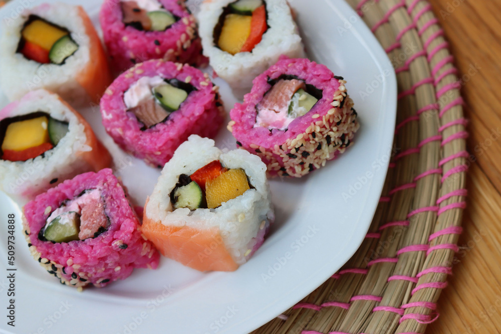 Japanese salmon sushi colored with beetroot juice with inside out rolls with fruits and vegetables on plate on wooden table Japanese salmon sushi colored with beetroot juice with inside out rolls with fruits and vegetables on plate on wooden table