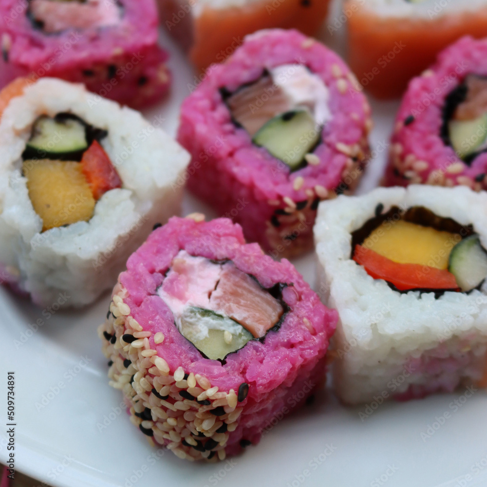 Japanese salmon sushi colored with beetroot juice with inside out rolls with fruits and vegetables on plate on wooden table Japanese salmon sushi colored with beetroot juice with inside out rolls with fruits and vegetables on plate on wooden table