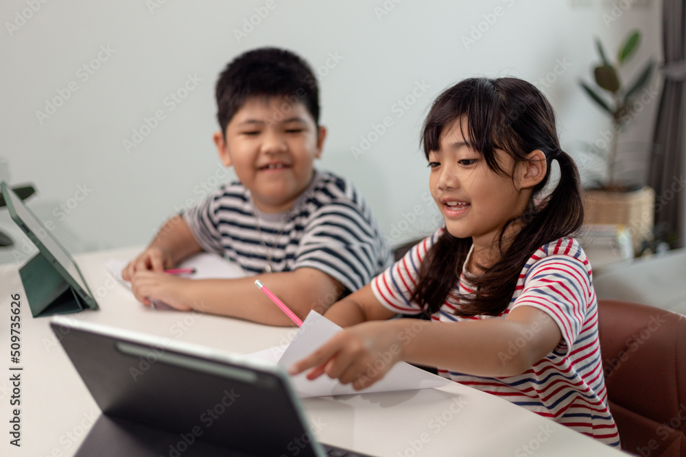 Asian boys and girls enjoy online learning by taking notes and using tablets at home. Asian boys and girls enjoy online learning by taking notes and using tablets at home.
