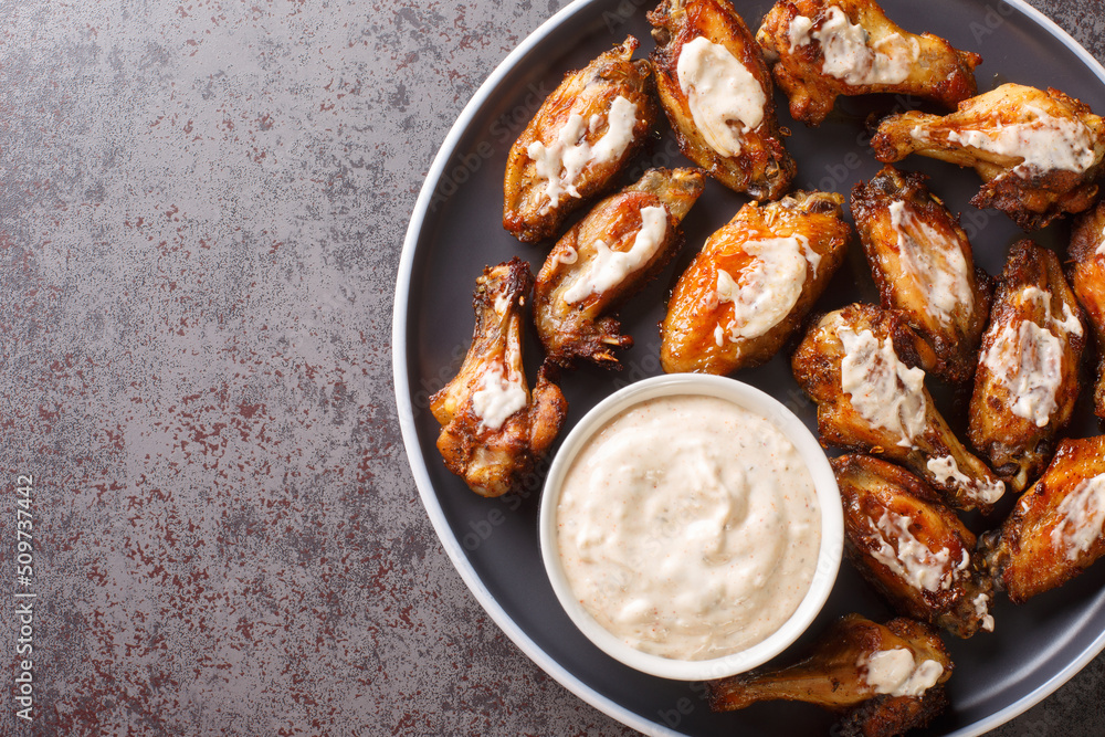 Tasty Chicken Wings with Alabama White Barbecue Sauce close-up in a plate on the table. Horizontal top view from above