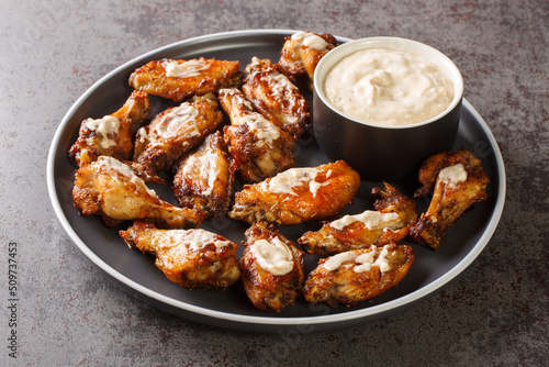 Portion of grilled chicken wings with Alabama white barbecue sauce close-up in a plate on the table. Horizontal