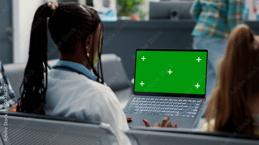 General practitioner holding laptop with greenscreen in waiting room, sitting in hospital reception lobby. Doctor using blank mockup template with isolated copyspace and chroma key. Tripod shot. General practitioner holding laptop with greenscreen in waiting room, sitting in hospital reception lobby. Doctor using blank mockup template with isolated copyspace and chroma key. Tripod shot.