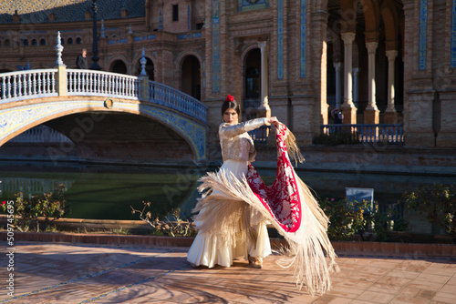 Flamenco dancer, woman, brunette and beautiful typical spanish dancer is dancing with a red manila shawl in a square in seville. Flamenco concept of cultural heritage of humanity.