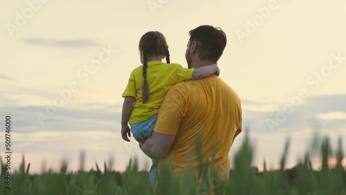 Agriculture. father carries child his arms. family walk through field with green wheat. farming. farmer walks across field with kid child daughter. growing green wheat. daddy care for child girl.