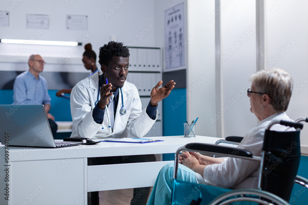 Fototapeta premium Physician expert explaining noninvasive procedure and treatment schedule to senior patient in wheelchair. Person with disability listening to hospital doctor talking about checkup appointment