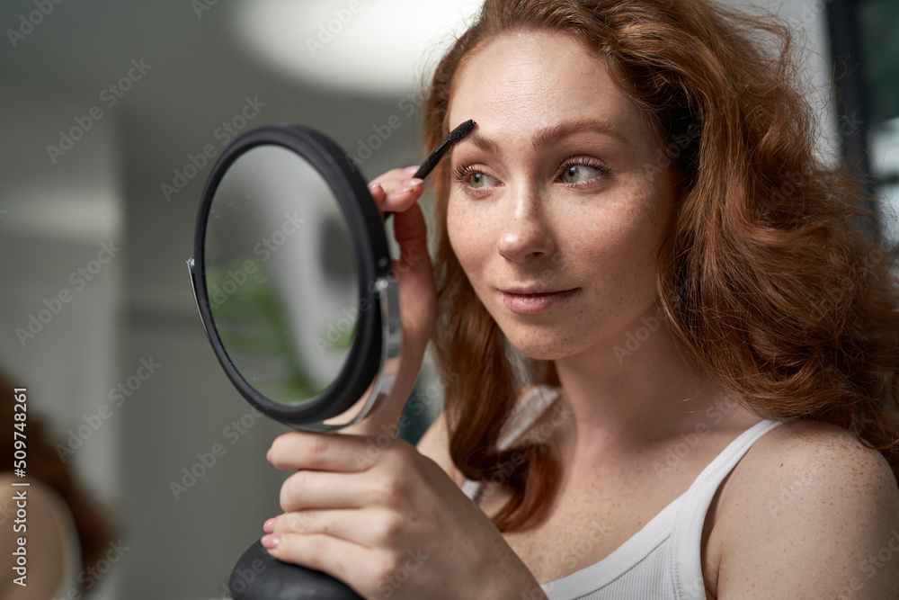Caucasian woman brushing eyebrows in the mirror reflection Caucasian woman brushing eyebrows in the mirror reflection