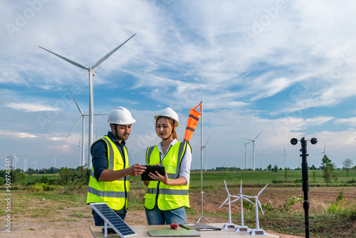 Engineer wearing uniform ,helmet inspection and survey work in wind turbine farms rotation to generate electricity energy. Green ecological power energy generation wind sustainable energy concept.