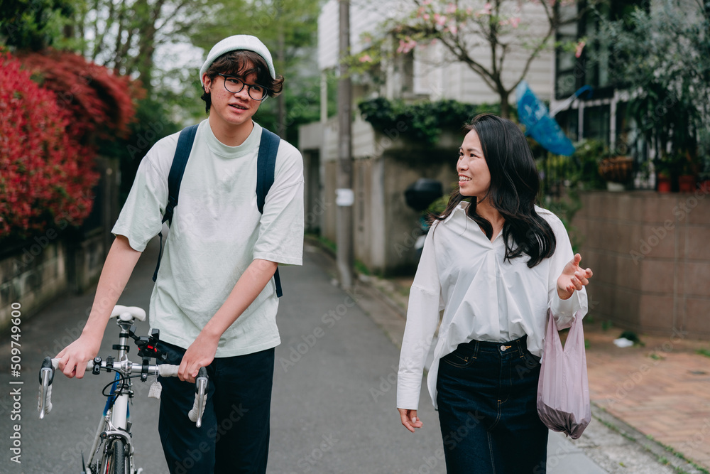 買い物から小さな住宅街を歩いて帰る母親と10代の息子 買い物から小さな住宅街を歩いて帰る母親と10代の息子