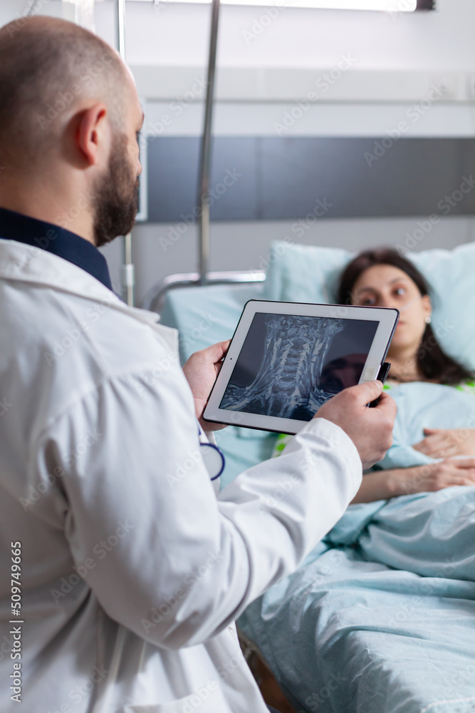Specialist doctor monitoring sick woman explaining bones radiography using tablet computer working in hospital ward. Patient resting in bed recovering after sickness surgery Specialist doctor monitoring sick woman explaining bones radiography using tablet computer working in hospital ward. Patient resting in bed recovering after sickness surgery