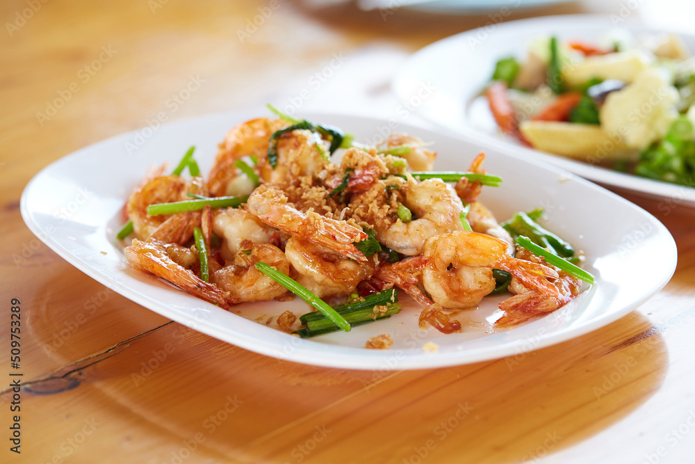 Fried shrimp with garlic and vegetables in white plate on wooden table, seafood.