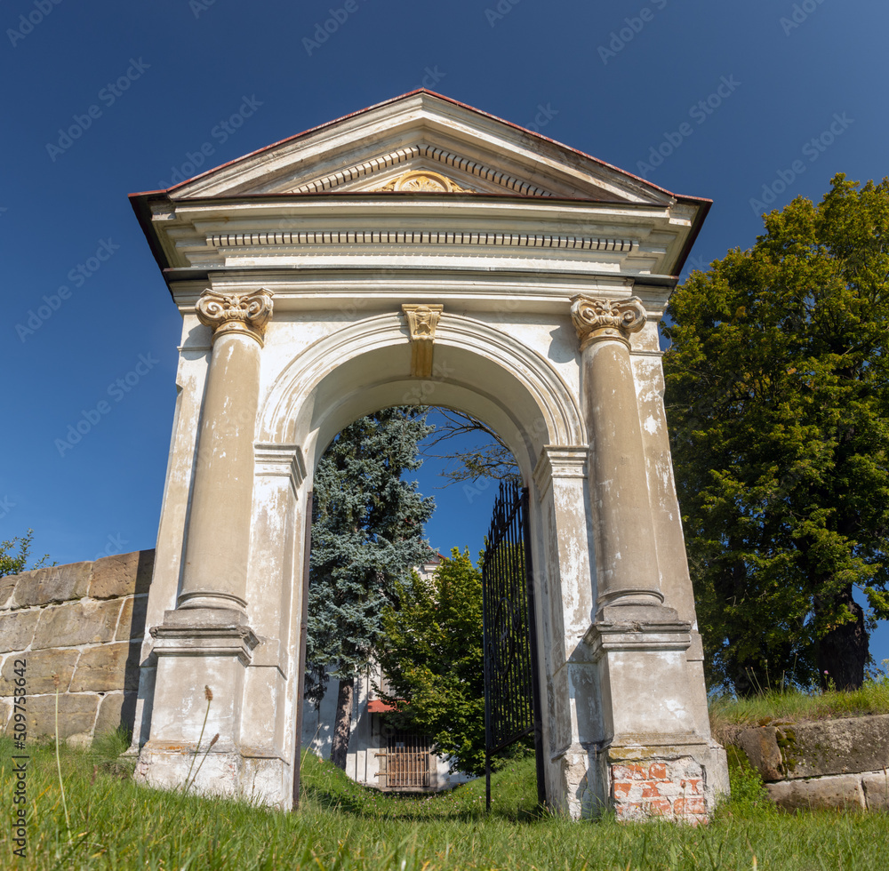 Classicist gate at the entrance to a country cemetery with a baroque chapel