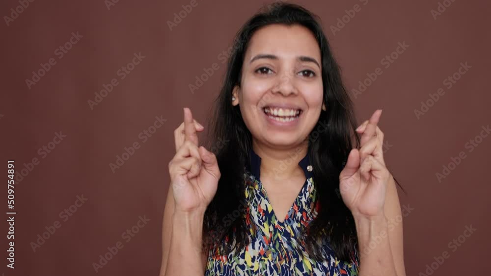 Indian woman holding fingers crossed for good luck in studio, feeling positive about success belief. Hopeful model waiting for miracle, wanting to fulfill wish with fortune, smiling. Indian woman holding fingers crossed for good luck in studio, feeling positive about success belief. Hopeful model waiting for miracle, wanting to fulfill wish with fortune, smiling.