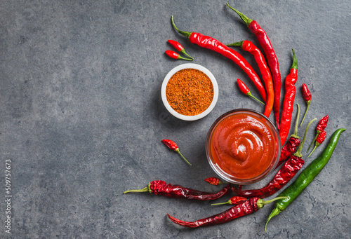Chili sauce ketchup in bowl and fresh chili peppers and dry flakes spices on dark background copy space. Spicy condiment.	