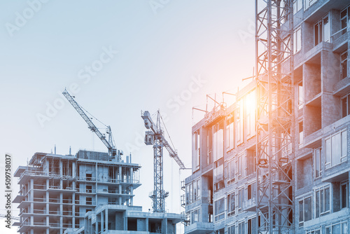 Foto Modern apartment residential building glass facade wall construction site with many high tower cranes and heavy machinery against blue sky background