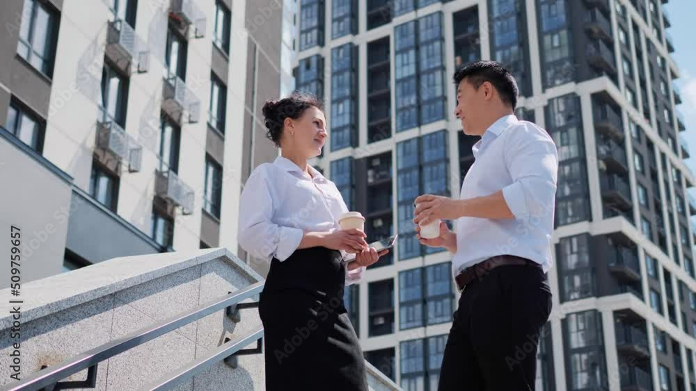 Two business people talking to each other discussing projects, work tasks for the day over morning coffee on the stairs. Asian businessman having conversation with a bank female employee outdoor. Two business people talking to each other discussing projects, work tasks for the day over morning coffee on the stairs. Asian businessman having conversation with a bank female employee outdoor.