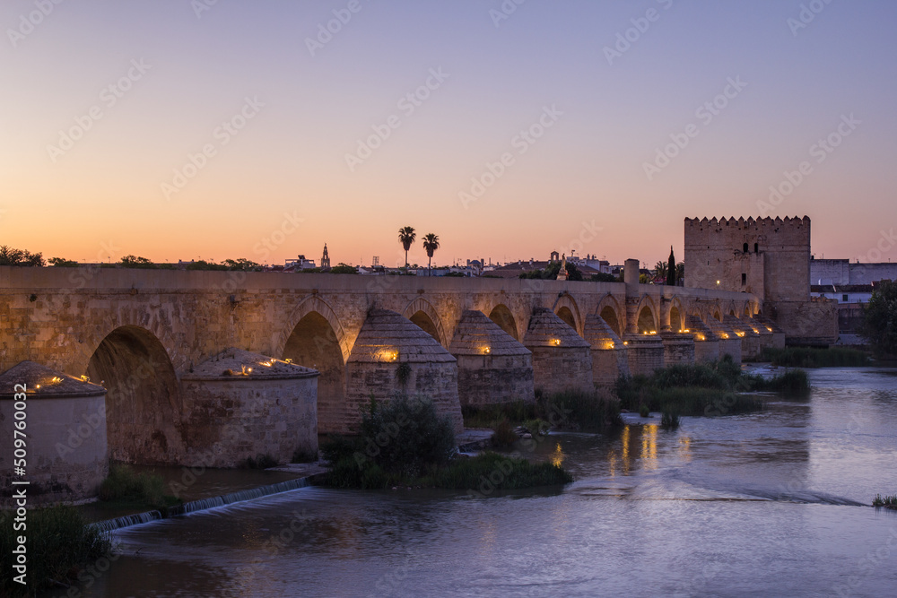 Ancient roman bridge across the Guadalquivir river in the morning twilight in the medieval city of Cordoba, Andalusia. Spain