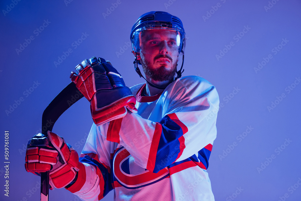 Obraz premium Closeup portrait of professional hockey player in sports uniform and protective equipment isolated on purple background in neon. Concept of sport, healthy lifestyle, hobby, movement, action.