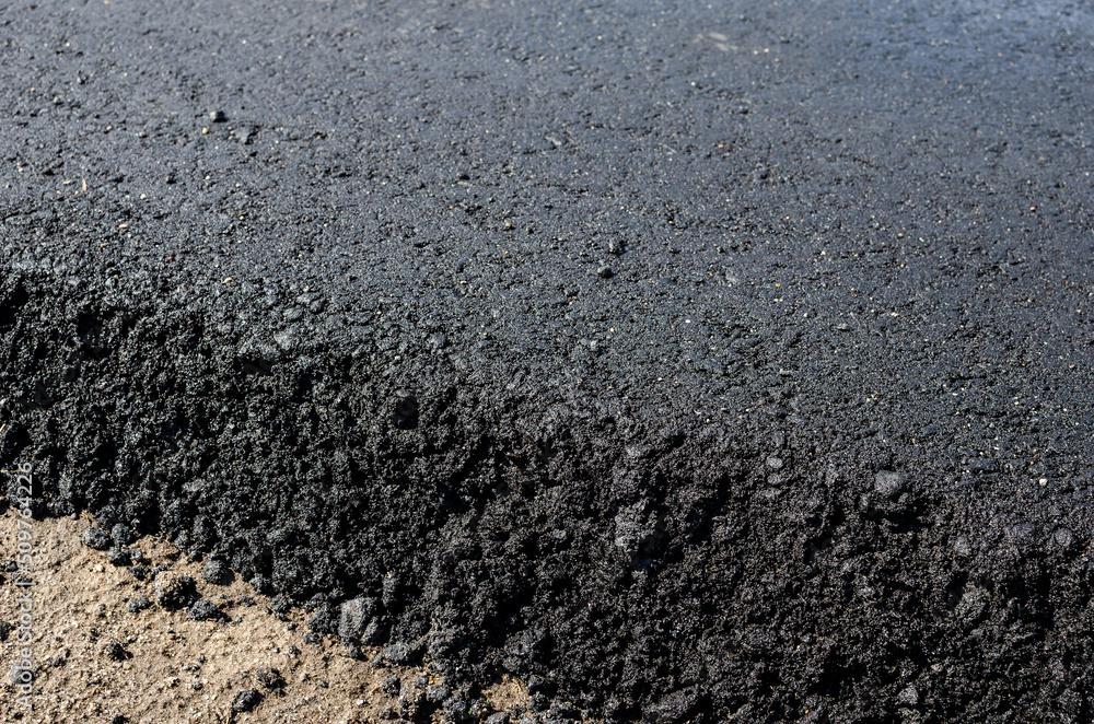 Fresh asphalt rolled by a vibrating road roller. Hot asphalt on a road construction site.