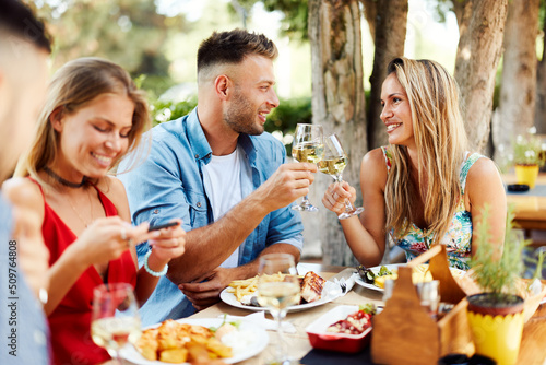 Group of Happy friends having lunch in the restaurant and toast with white wine during a sunny summer day