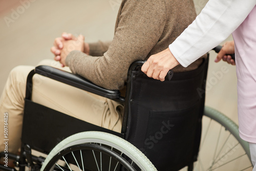 Close-up of unrecognizable medical nurse pushing wheelchair with disabled patient while they walking outdoors