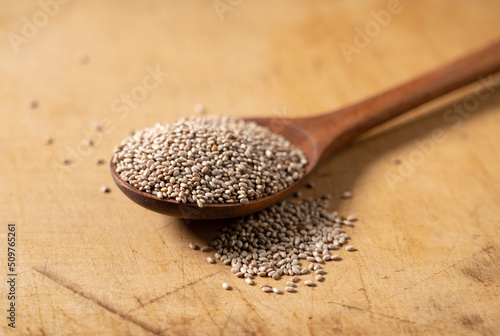 Wooden spoon and white chia seeds placed on wooden background.