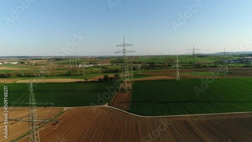 Electric supports against the sky among empty green and yellow square fields. The civilization is visable on the background, cars are driving on a asphalt road. Sunny day, summer, countryside, high photo