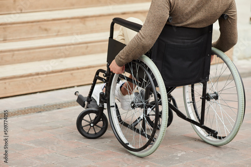 Close-up of unrecognizable crippled man in sweater turning handrails while moving wheelchair outdoors