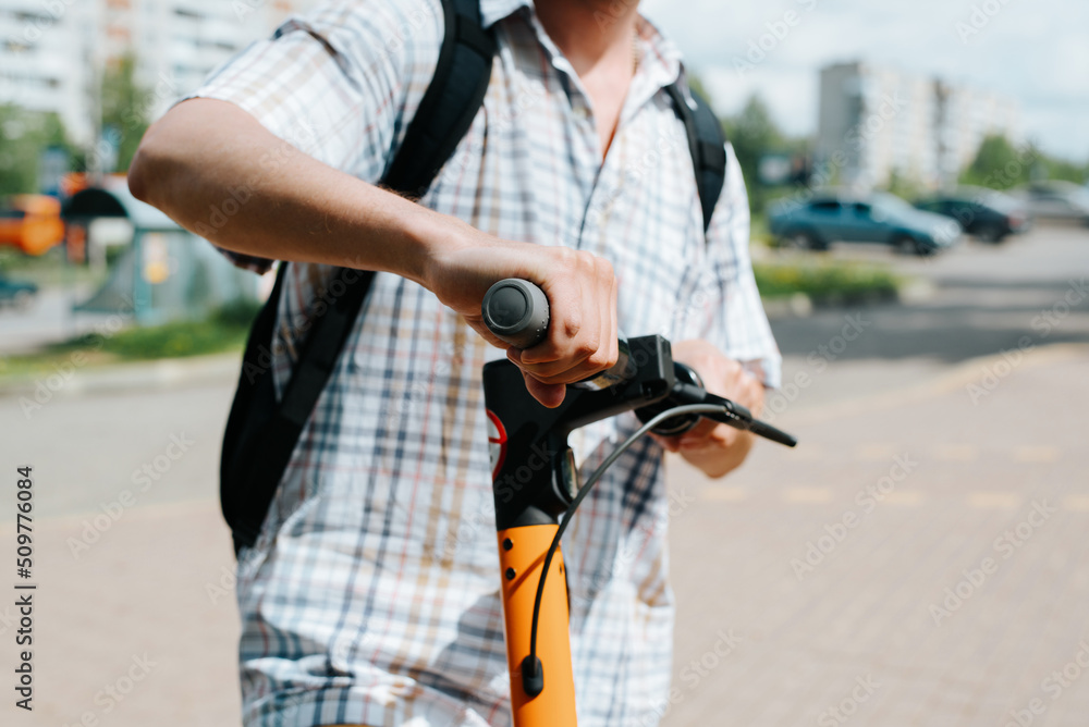 Close-up of man driving rented electric scooter outdoors. Selective focus on male hand holding steering wheel of vehicle, side view Close-up of man driving rented electric scooter outdoors. Selective focus on male hand holding steering wheel of vehicle, side view