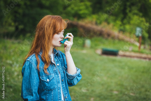 Woman using asthma inhaler in a park. Portrait of young handsome woman using asthma inhaler. She using a pressurized cartridge inhaler extended pharynx