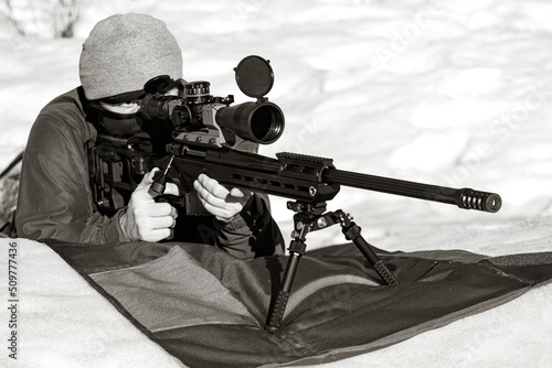 A sniper rifles with an optical sight in man`s hands aiming laying winter day photo