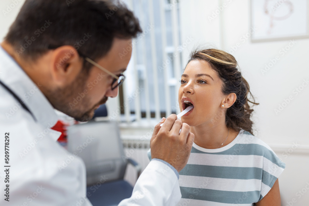 Doctor using inspection spatula to examine patient throat. ENT doctor doing throat exam of a woman. patient opened her mouth to throat check-up Doctor using inspection spatula to examine patient throat. ENT doctor doing throat exam of a woman. patient opened her mouth to throat check-up