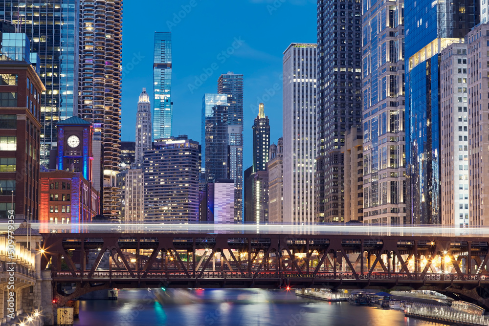 Fototapeta premium Railway bridge over Chicago River amidst illuminated city. Urban skyline with skyscrapers at night. .