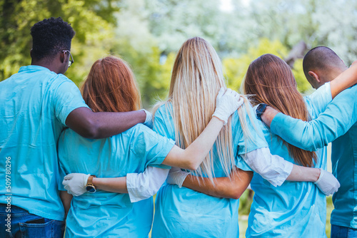 Diverse group of friends cleanup a park during a charity event. They are standing with their arms around one another.....