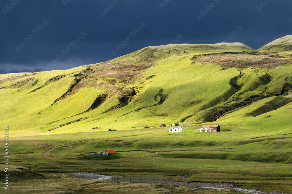 Sunshine with dark clouds over a farm in the mountain, scenic landscape in Iceland
