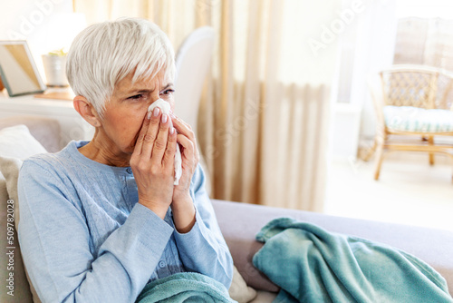Photos Shot of a senior woman blowing her nose with a tissue at home