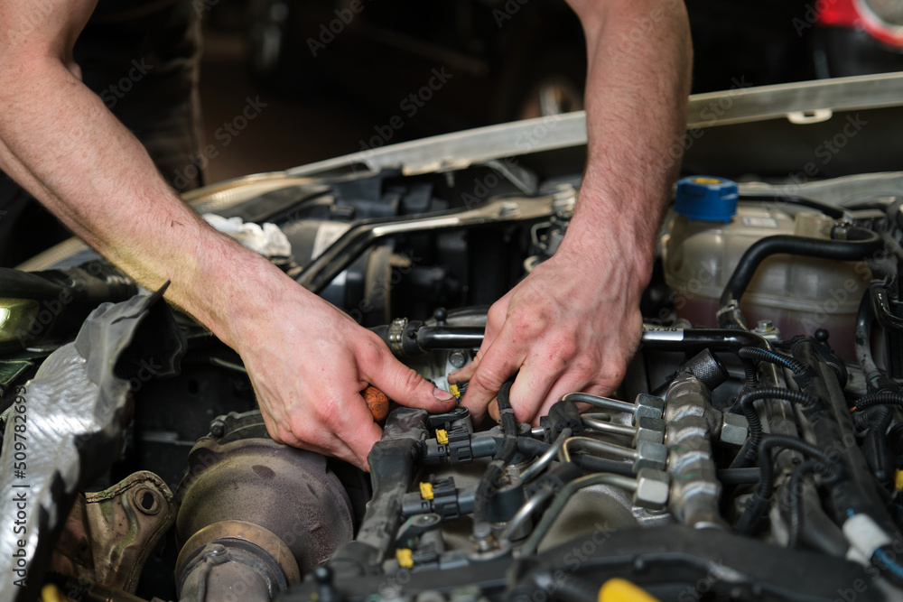 Close up of car mechanic hands removing fuel injectors in engine room checking dust and test pressure in maintenance process.