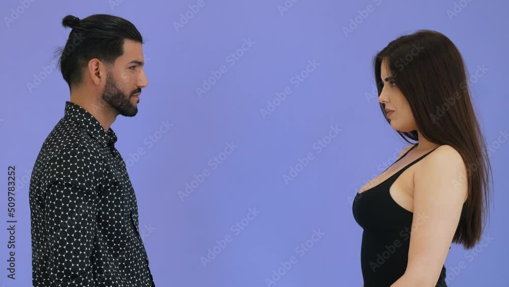 Two attractive people - a long-haired woman and a bearded man - standing face to face. Intense emotions without any words. Violet background isolated copy space studio shot. High quality 4k footage Two attractive people - a long-haired woman and a bearded man - standing face to face. Intense emotions without any words. Violet background isolated copy space studio shot. High quality 4k footage