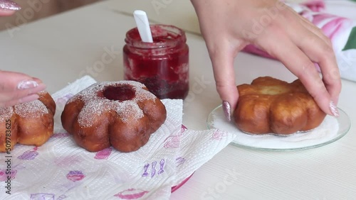 A woman dips a donut in powdered sugar. Puts jam on donuts. Prepares donuts in the form of a flower. Close-up. photo