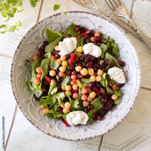 plate with salad with baked beets, chickpeas and pomegranate on a light table
