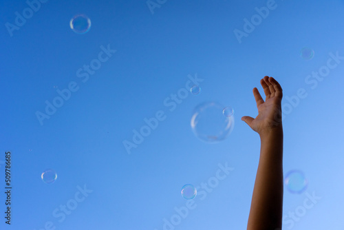 Hand of a child trying to catch some soap bubbles that rise to the sky © JoseLuis