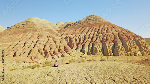 Meditation among the colored mountains. Limestone mountains in the middle of the desert. Colored hills from white to red. The guy sits and contemplates the nature of the Altyn Emel canyon. Kazakhstan.