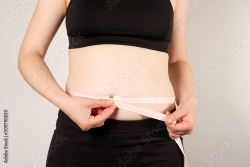 A woman measures the circumference of the abdomen with a centimeter tape, close-up. Slimming concept